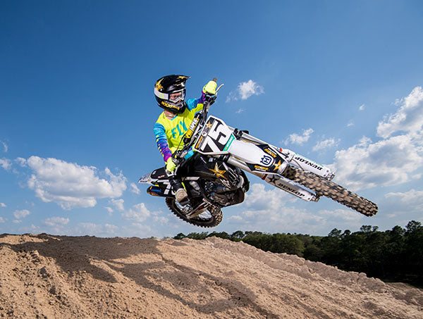 White Husqvarna dirt bike doing a table top jump - mobile optimized